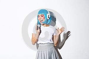 Image of beautiful asian girl in blue wig sinting into mobile phone dynamic, wearing headphones, playing karaoke app