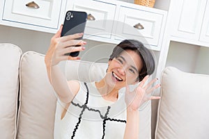 Image of beautiful asian woman laughing and showing peace sign while taking selfie photo on cellphone