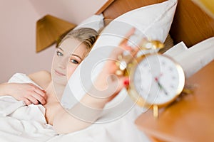 Image of beautiful blond young business woman blue eyes girl touching alarm clock off wake up time looking at camera happy smiling