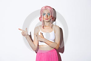 Image of beautiful caucasian girl in pink party wig and bright makeup pointing fingers left at your logo, showing banner