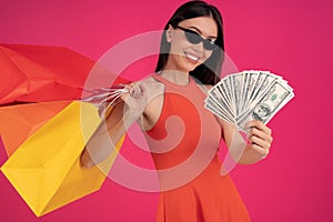 Image of a beautiful excited happy asian woman posing isolated over pink wall background holding shopping bags and money. dressed