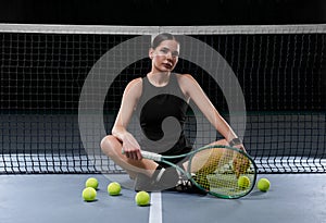 Image of a beautiful female tennis player in a black dress posing on the tennis court. Sports concept