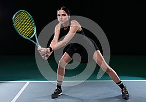 Image of a beautiful female tennis player in a black dress posing on the tennis court. Sports concept