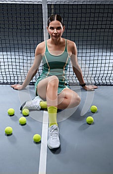 Image of a beautiful female tennis player in a green dress posing on the tennis court. Sports concept