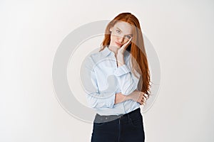 Image of beautiful girl student in blue shirt looking annoyed or bored, leaning face on palm and sulking at camera