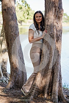 Image of a beautiful happy woman posing next to a tree by the lake