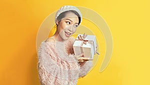 Image of a beautiful happy young asian woman posing isolated over yellow wall background holding present gift box