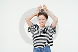 Image of beautiful, happy young woman showing bunny ears on top of her head, looking excited, posing over white