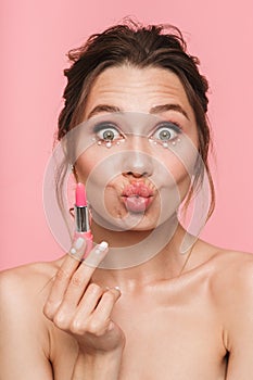 Shocked happy young woman posing isolated over pink wall background holding lipstick