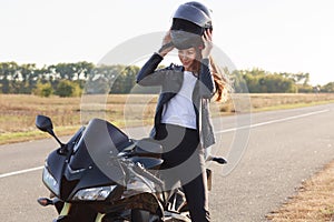 Image of beautiful slender young risk taker sitting on her motorcycle, having trip on her vehicle, fond of extreme activities,