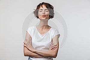 Image of beautiful woman in basic t-shirt looking at camera while standing with arms crossed