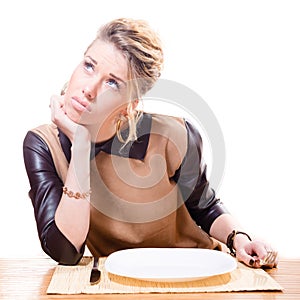 image of beautiful young attractive blond woman holding fork in her hand looking up, empty plate isolated on white background