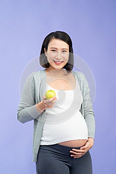 Image of a beautiful young pregnant woman posing isolated over purple wall background holding apple eat healthy food