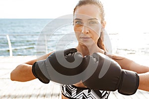 Beautiful young sports fitness woman boxer make exercises in gloves at the beach outdoors