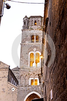 Image of a bell tower near a church with illuminated windows, captured in Caserta Vecchia, Italy