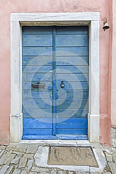 Image of a blue wooden entrance door to a building with an antique faÃ§ade