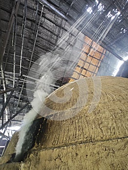 bright smoke streaming from charcoal kiln outlet to the ceiling attap roof hole. photo