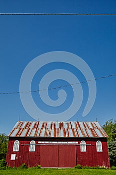 Broad side of a white and red barn with trees, blue sky, and power lines in the background