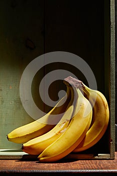 Image of bunch of ripe yellow bananas on wooden background, bright sunlight, harvest in wooden box