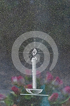 Image of a burning candle on a granite tombstone with a reflection of wreath flowers. Halloween.