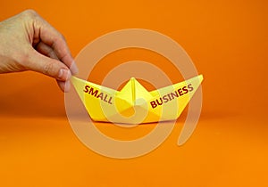 Image of businessman pushing paper made origami boat forward in a conceptual image. Text `small business`. Over orange backgroun