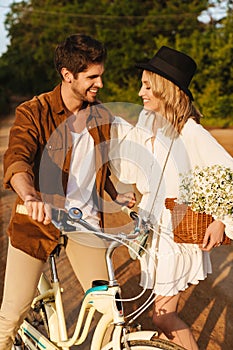 Image of caucasian couple smiling and riding bicycle in countryside
