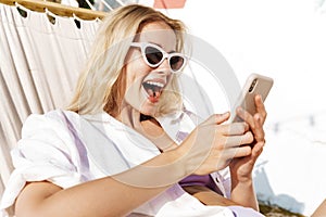Image of charming excited woman using cellphone while lying in hammock