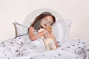 Image of charming magnetic little infant sleeping in her light bedroom alone, lying in soft cosy bed, hugging her favourite bear