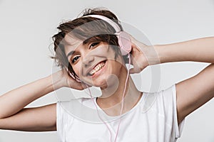 Image of charming woman in basic t-shirt looking at camera while listening to music with headphones