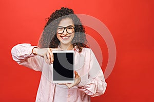 Image of cheerful amazed young curly caucasian woman showing display of tablet computer