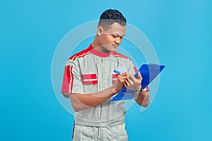 Image of cheerful asian handsome man wearing mechanic uniform taking notes on clipboard