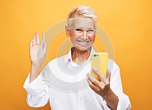 Image of cheerful mature old woman standing isolated over yellow background wall talking by mobile phone