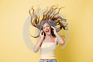 Image of cheerful woman 20s singing and enjoying tune with shaking hair while listening to music via headphones, isolated over ye