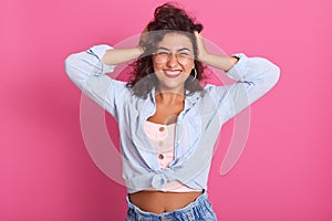Image of cheerful young beautiful woman standing  over pink background in studio, keeping her hands on head, laughing