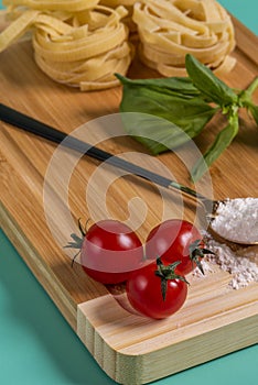 Image of cherry tomatoes in the foreground on a bamboo table with flour, basil and pasta in the background