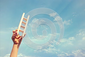 Image of child hand holding a ladder against the sky. education and success concept.