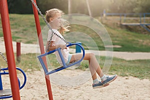 Image of child on swing in playground outdoors, liitle girl with ponytail and casual clothing, looking away with concentarted