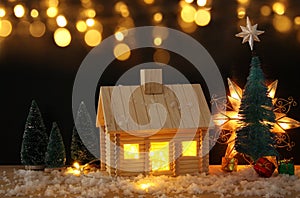 Image of christmas tree and wooden house with light through the window, over snowy table.