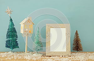 Image of christmas trees next to empty photo frame on snowy wooden table. For photography montage.