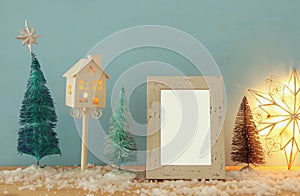 Image of christmas trees next to empty photo frame on snowy wooden table. For photography montage.