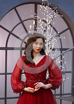 Image of a Christmas witch, a delightful red dress adorned with flowers and sleeves, a girl with warm wavy hair, a New
