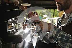 Image closeup of bearded barista man making coffee while working in cafe or coffeehouse outdoor