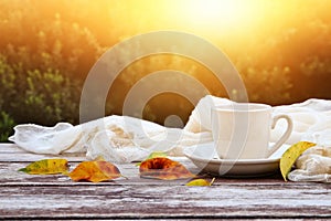 image of coffee cup over wooden table and autumn leaves in front of autumnal background