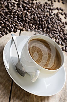 Image of a coffee cup and saucer with an old vintage spoon on a wooden table top. surrounded by raw coffee beans, taken at an