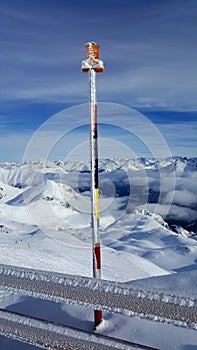 Image of a colorful frozen stick with orange alarm light on the peak of a mountain in a ski resort in the snowy alps