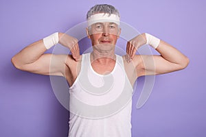Image of concentrated energetic man standing isolated over lilac background in studio, raising arms, doing physical exercises,