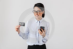 Image of confident office woman wearing eyeglasses holding mobile phone and credit card, isolated over white background