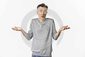 Image of confused middle-aged man shrugging shoulders, looking clueless at camera, standing over white background