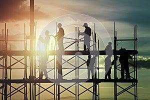 Image Construction workers on scaffold working in intense sunlight, shadowed silhouette