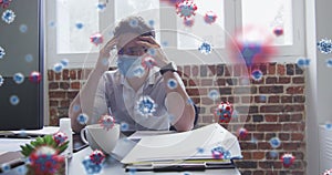 Image of covid 19 cells over stressed man in face mask, holding his head in office